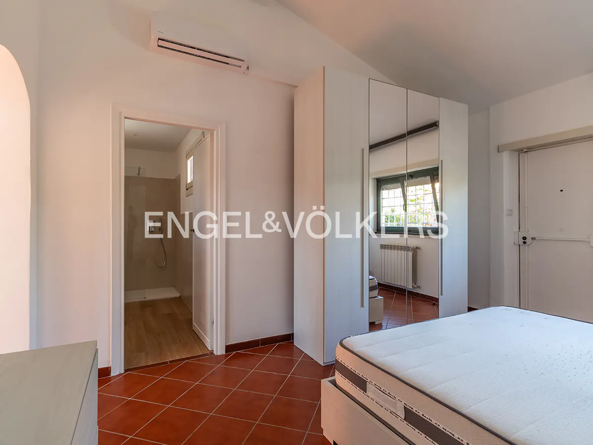 Bedroom with white walls, terracotta tile floor, bed, mirrored closet, and bathroom doorway.