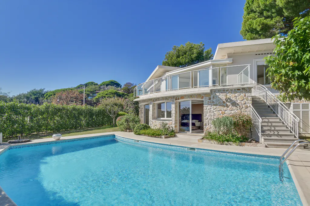 Exterior view of a stone house with a blue swimming pool and a staircase leading to the second floor.
