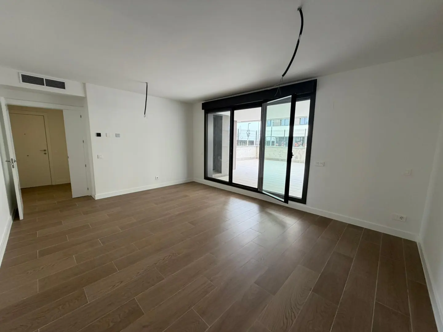 An empty room with wood floors, white walls, and a sliding glass door to a balcony.