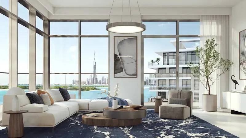 Bright living room with floor-to-ceiling windows overlooking Dubai skyline. White sectional sofa, blue rug, and modern decor.