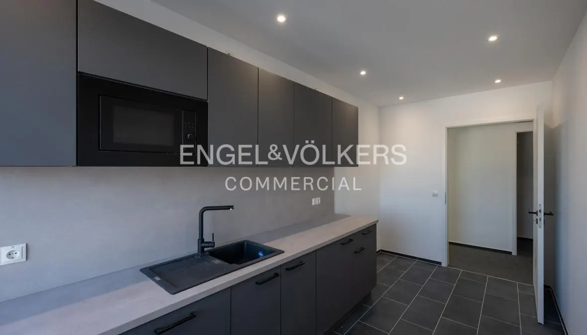 Modern kitchen with matte grey cabinets, light grey countertops, a black sink, and dark tiled flooring.
