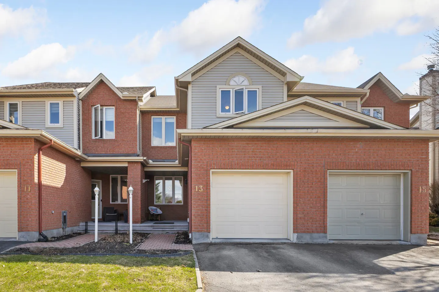 A townhouse with a red brick facade, light gray siding, and two garage doors under a blue sky.