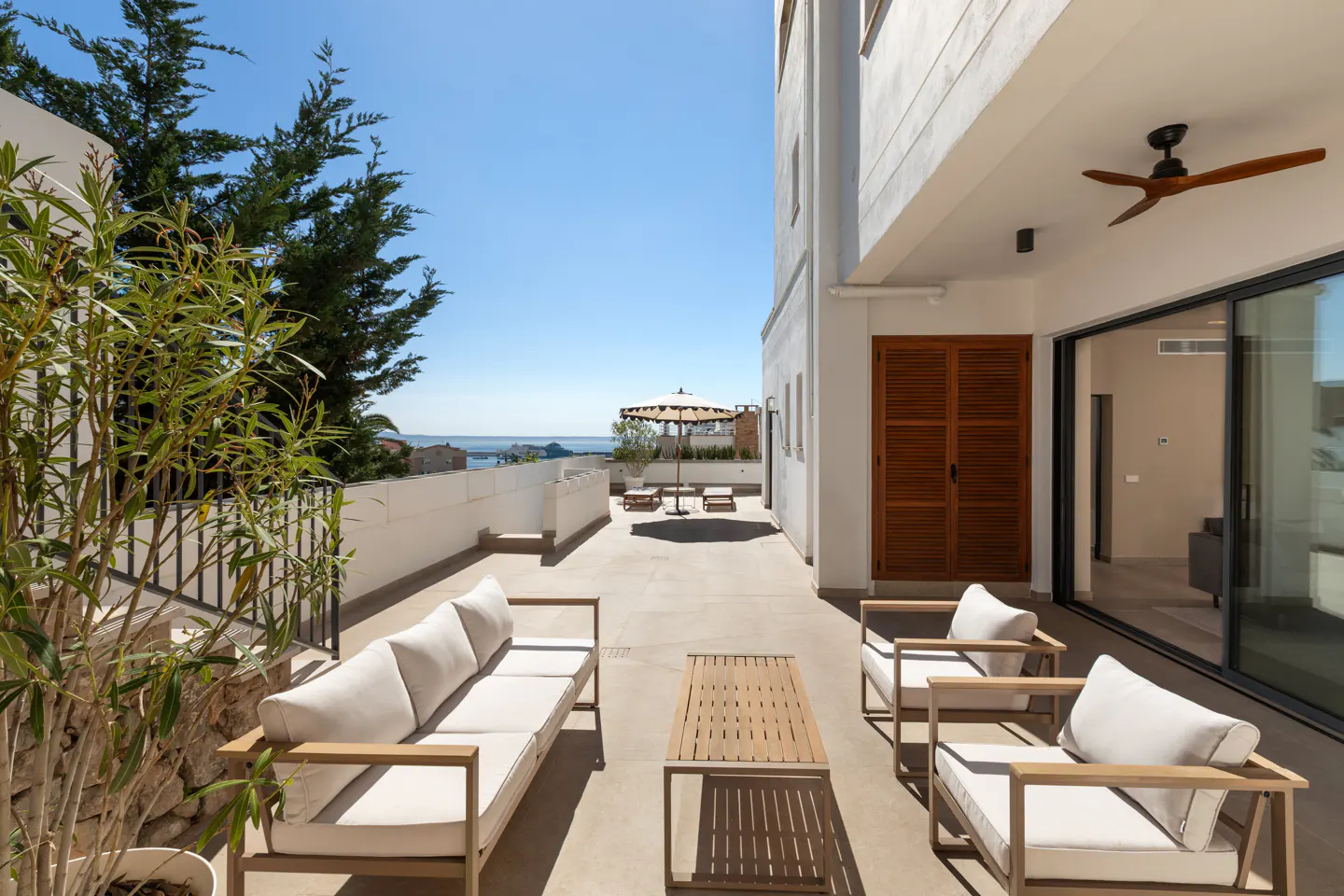Outdoor patio with a sofa, two chairs, and a table. Ocean view with an umbrella and lounge chairs in the background.
