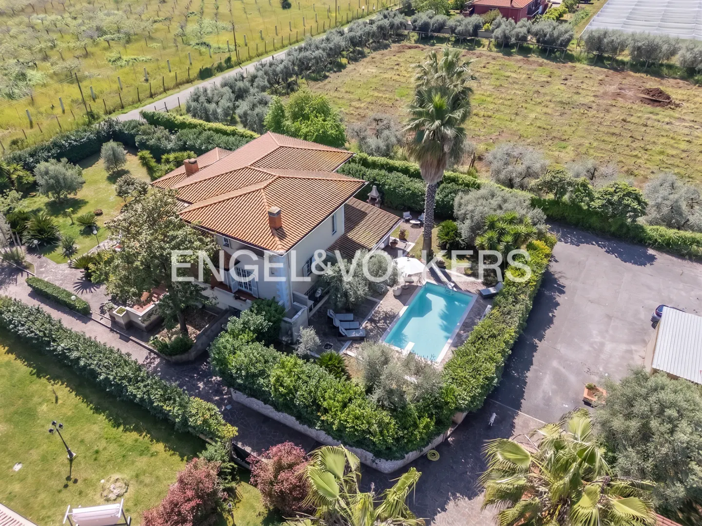 Aerial view of a light-colored house with a red tile roof, a pool, and the Engel & Volkers logo.
