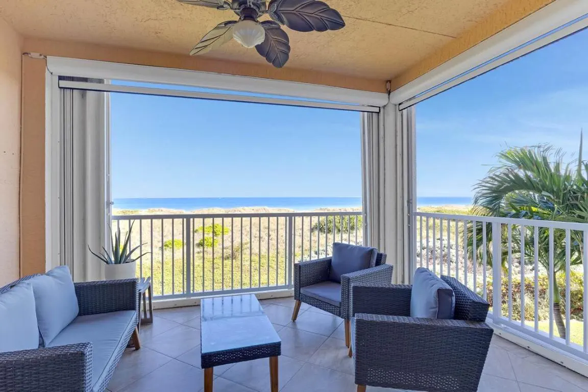 Balcony with wicker furniture overlooks a beach and ocean view. A ceiling fan is visible above.