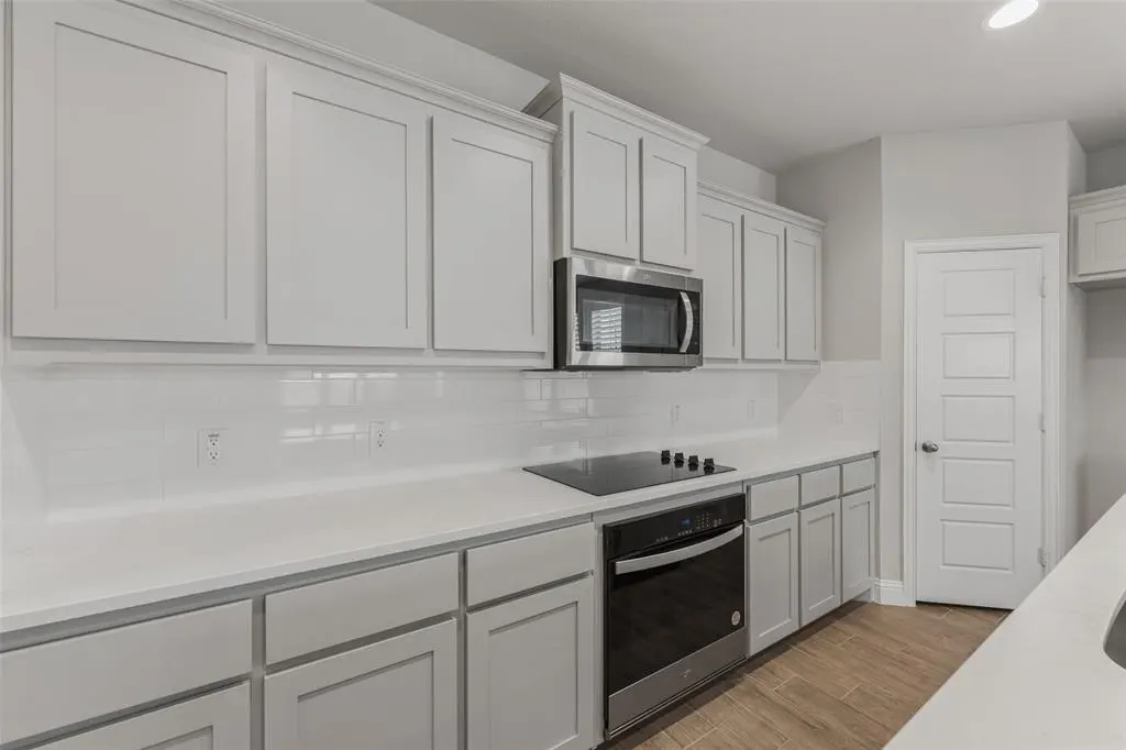 Bright kitchen with white cabinets, quartz countertops, stainless steel microwave, and black cooktop. Wood-look tile floor.