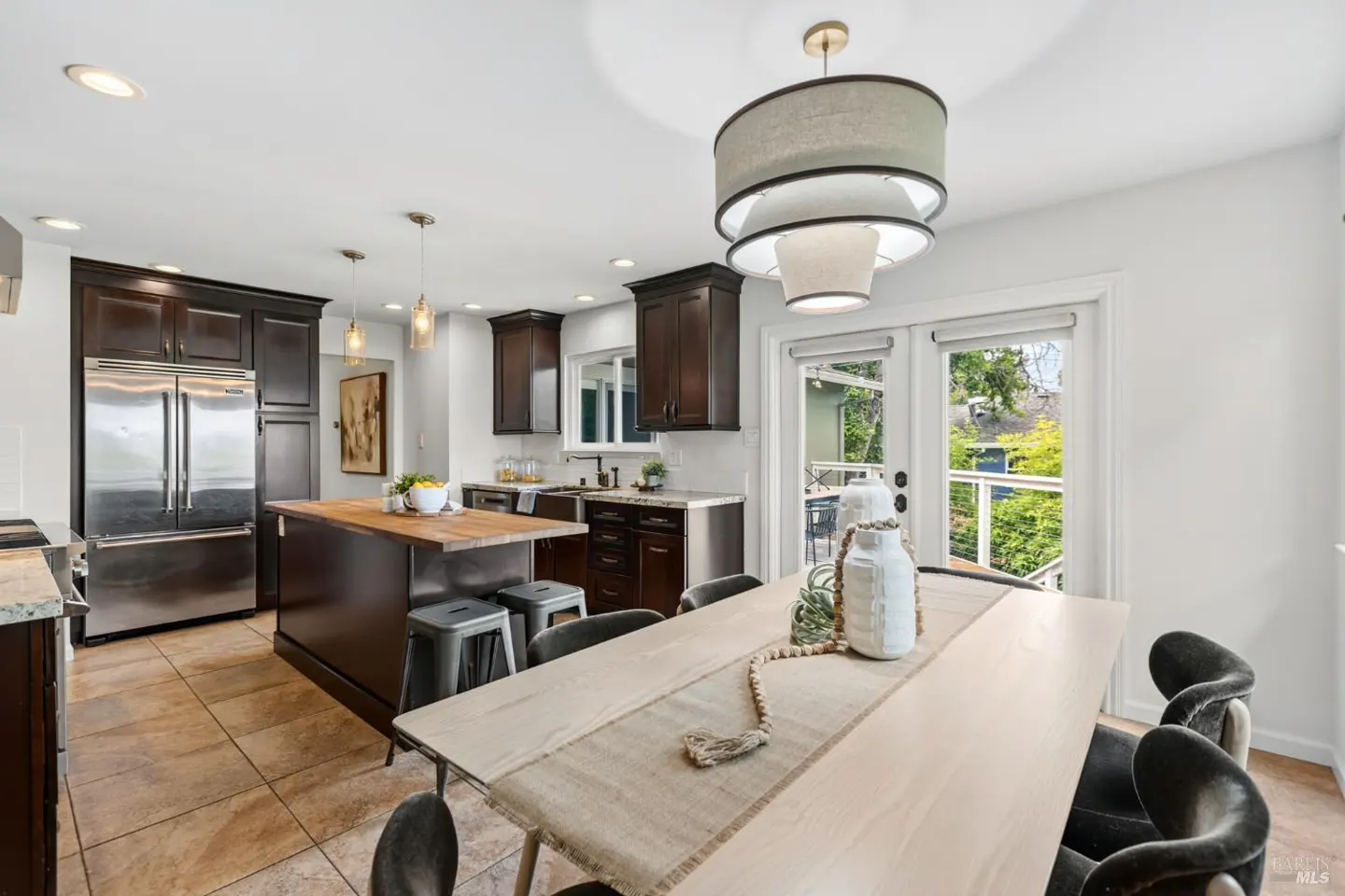 Modern kitchen with dark wood cabinets, stainless steel appliances, a wooden island, and a dining table with grey chairs.