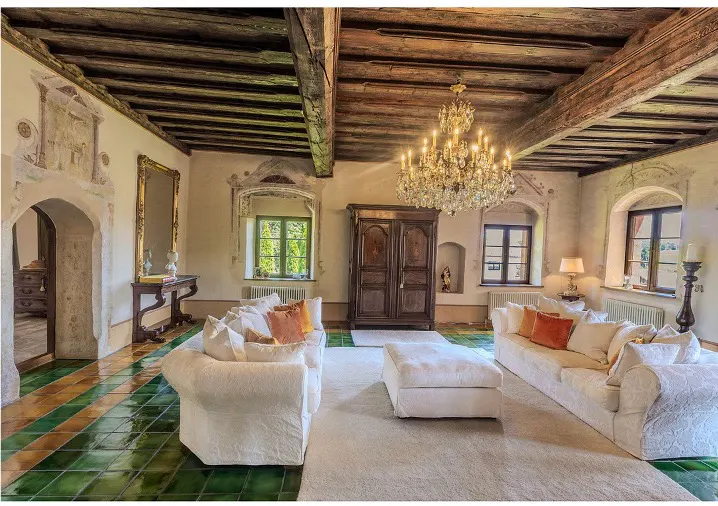 Living room with white sofas, orange pillows, and a large chandelier. The floor is tiled in green and gold.