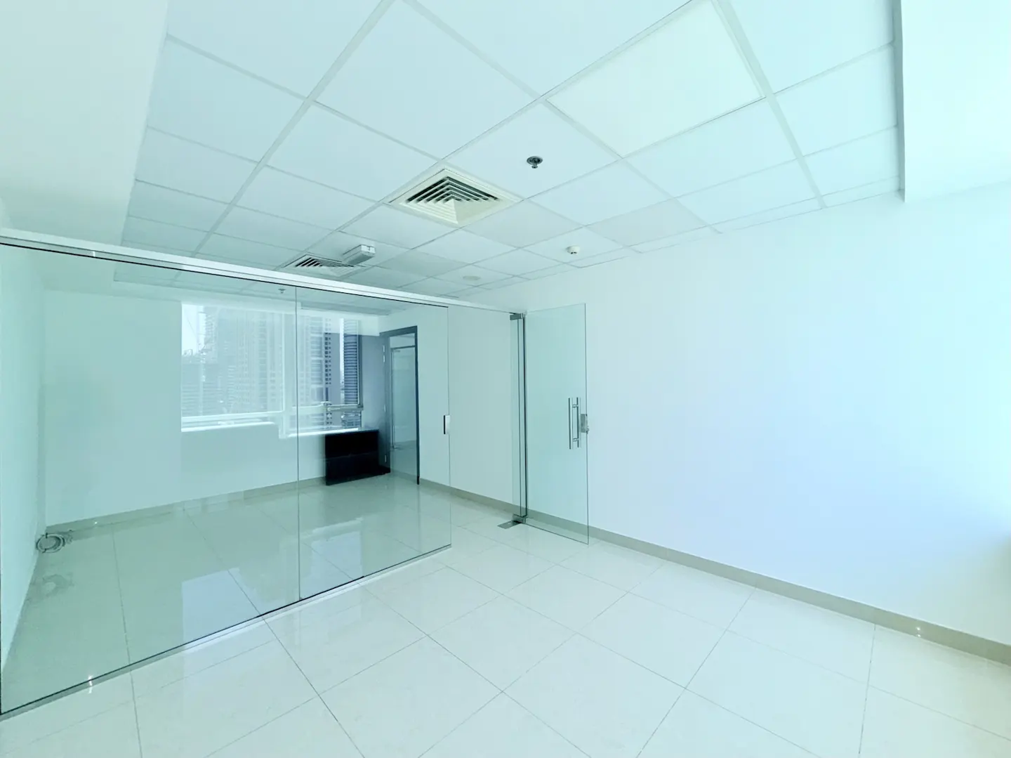 Bright, empty office space with white walls, tiled floor, and glass-walled room.