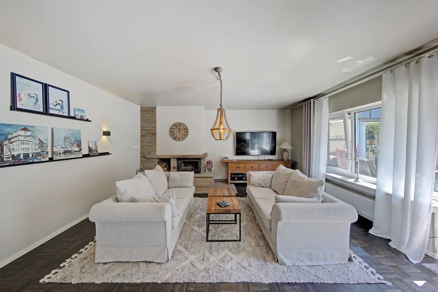 Living room with two white sofas facing each other, a fireplace, and a TV. A light fixture hangs from the ceiling.