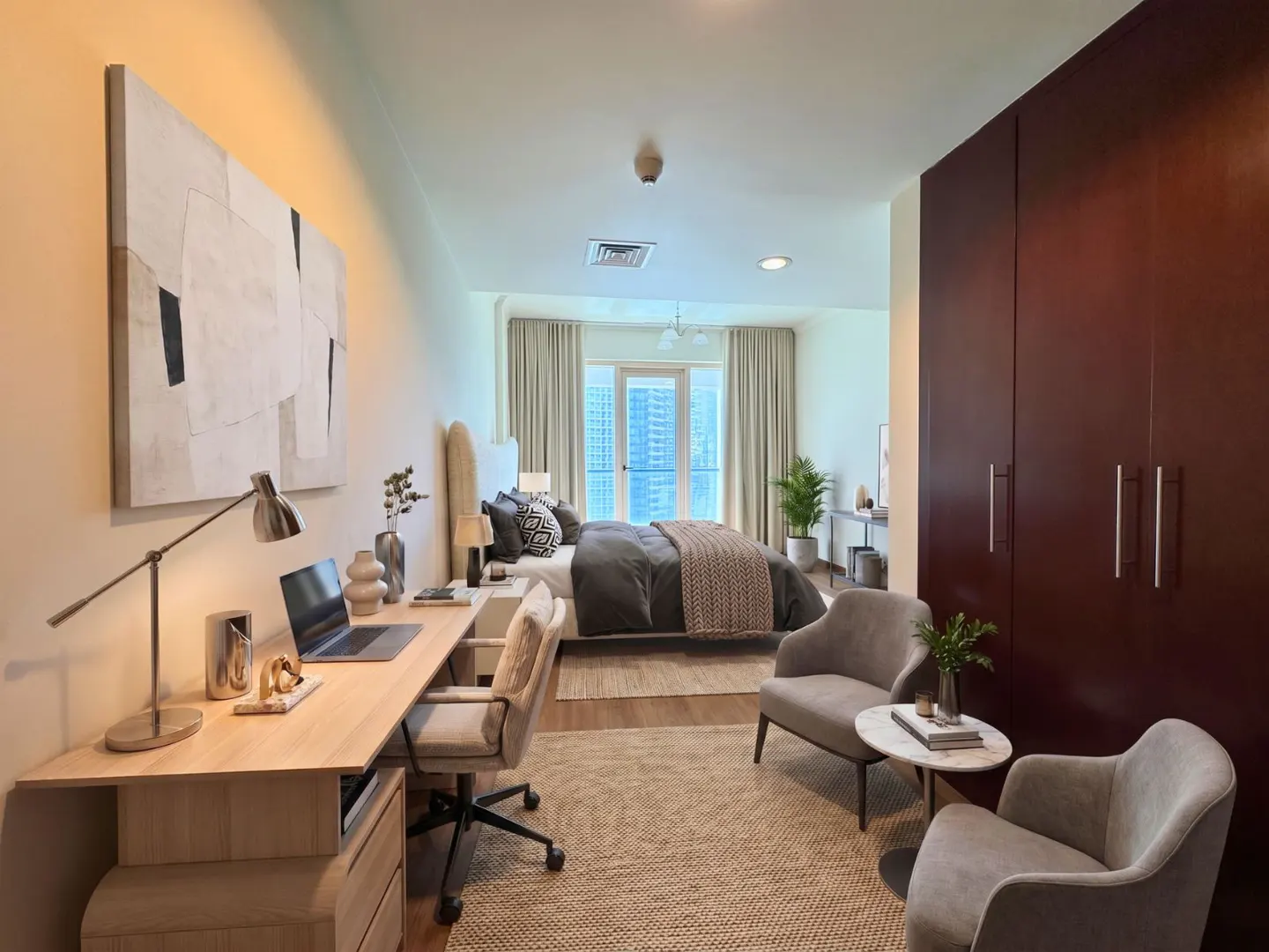 Bedroom with a desk, bed, and seating area. A large abstract painting hangs above the desk. The room has a neutral color palette with pops of brown.