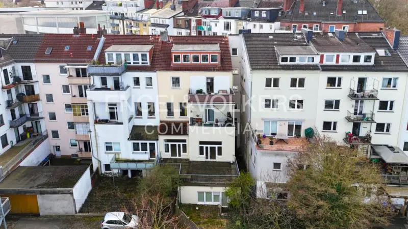 Aerial view of multi-story buildings with red and gray roofs, white and beige facades, and a small car parked in front.