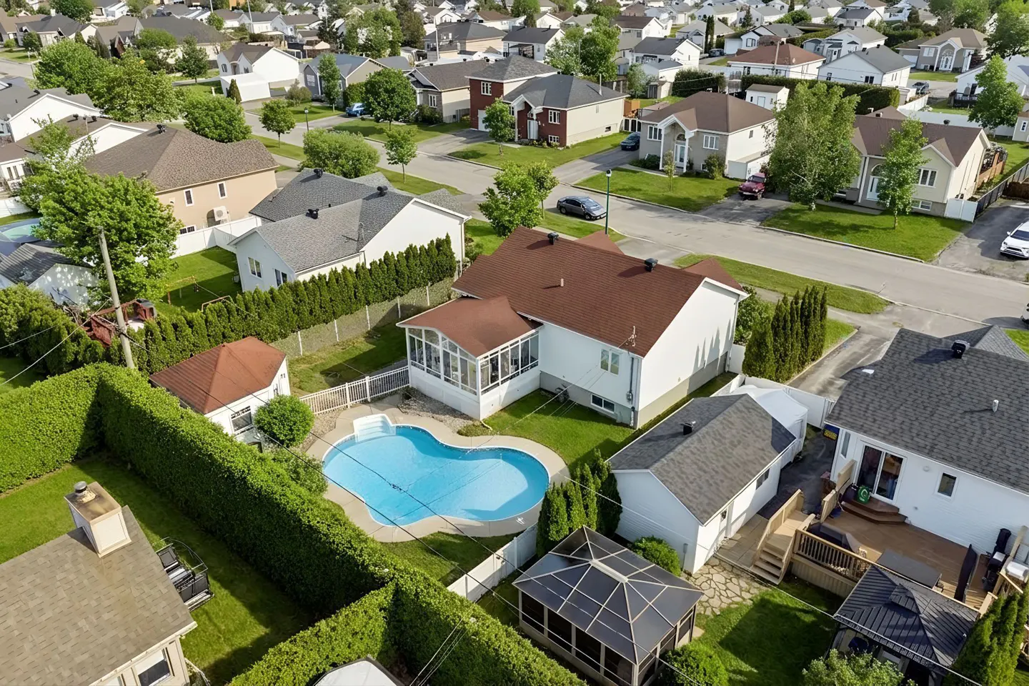 Aerial view of a suburban home with a kidney-shaped pool, sunroom, and backyard gazebo in a quiet residential neighborhood.