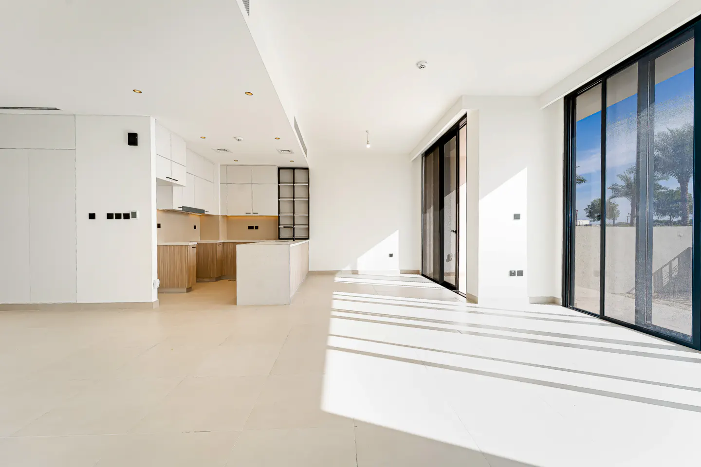 Modern open-plan living area with white walls, light tile floors, and a sleek kitchen with wood-toned cabinets.