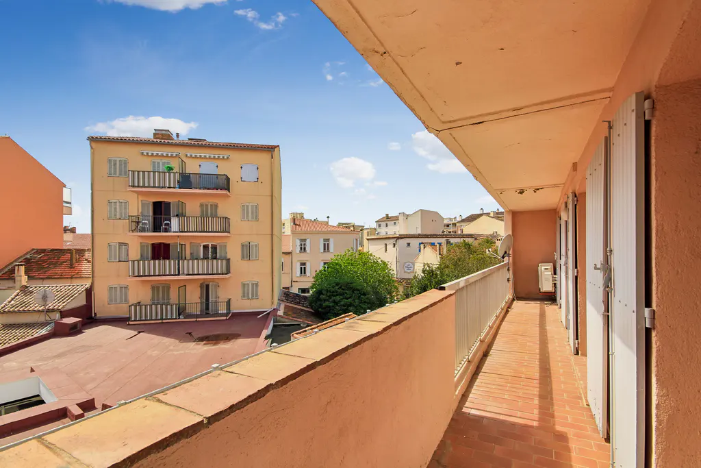 View from a peach-colored balcony with white shutters, overlooking a courtyard and buildings under a blue sky.