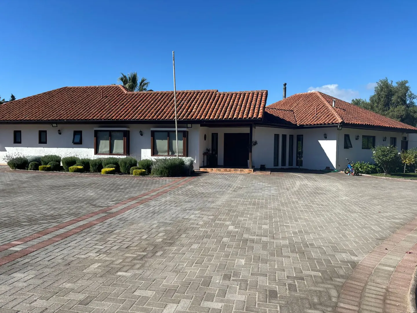A white, single-story house with a red tile roof and a brick driveway under a clear blue sky.