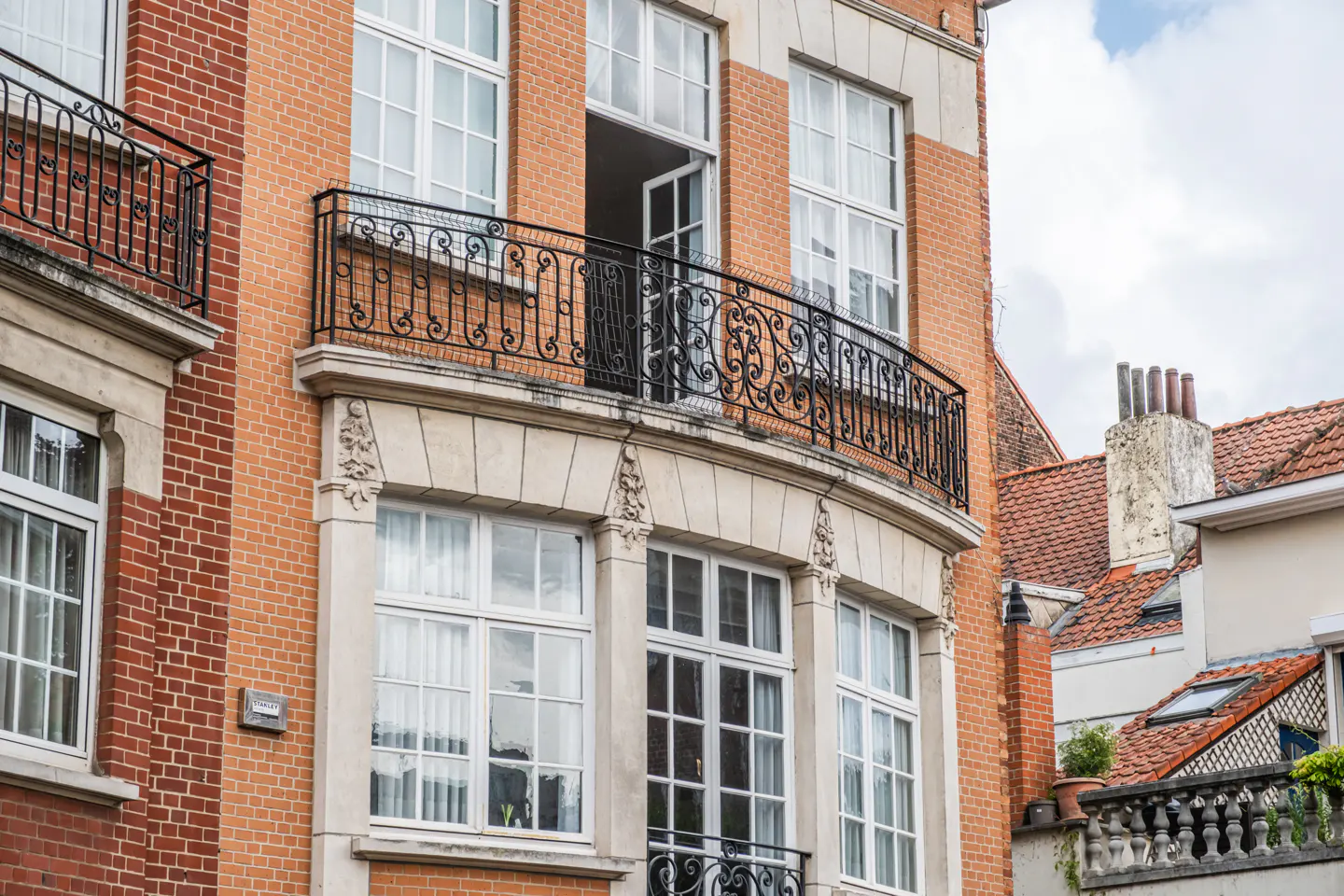 Brick building with white-framed windows and black wrought-iron balconies. One window is open.