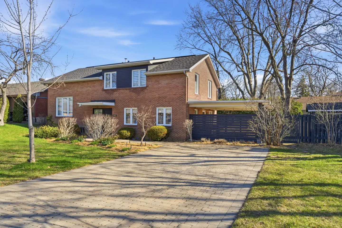 Brick house with white windows and a dark blue accent wall above the front door, a stone driveway, and green grass.