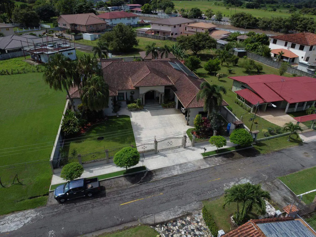 Aerial view of a tan house with a red tile roof, a gated driveway, and a black truck parked on the street.