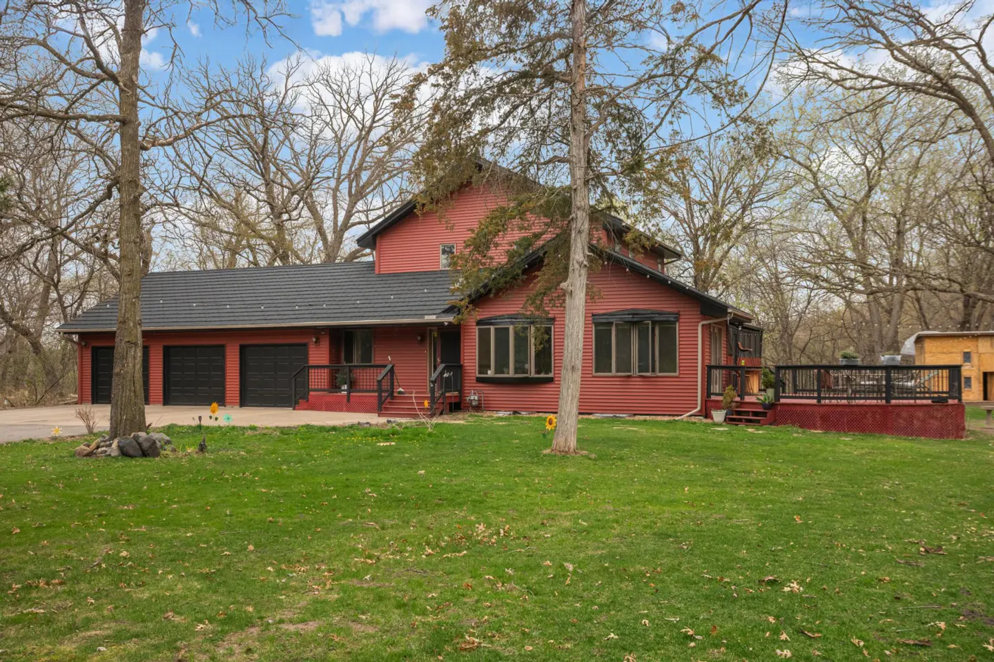 A red two-story house with a black roof and a two-car garage, surrounded by trees and a green lawn.