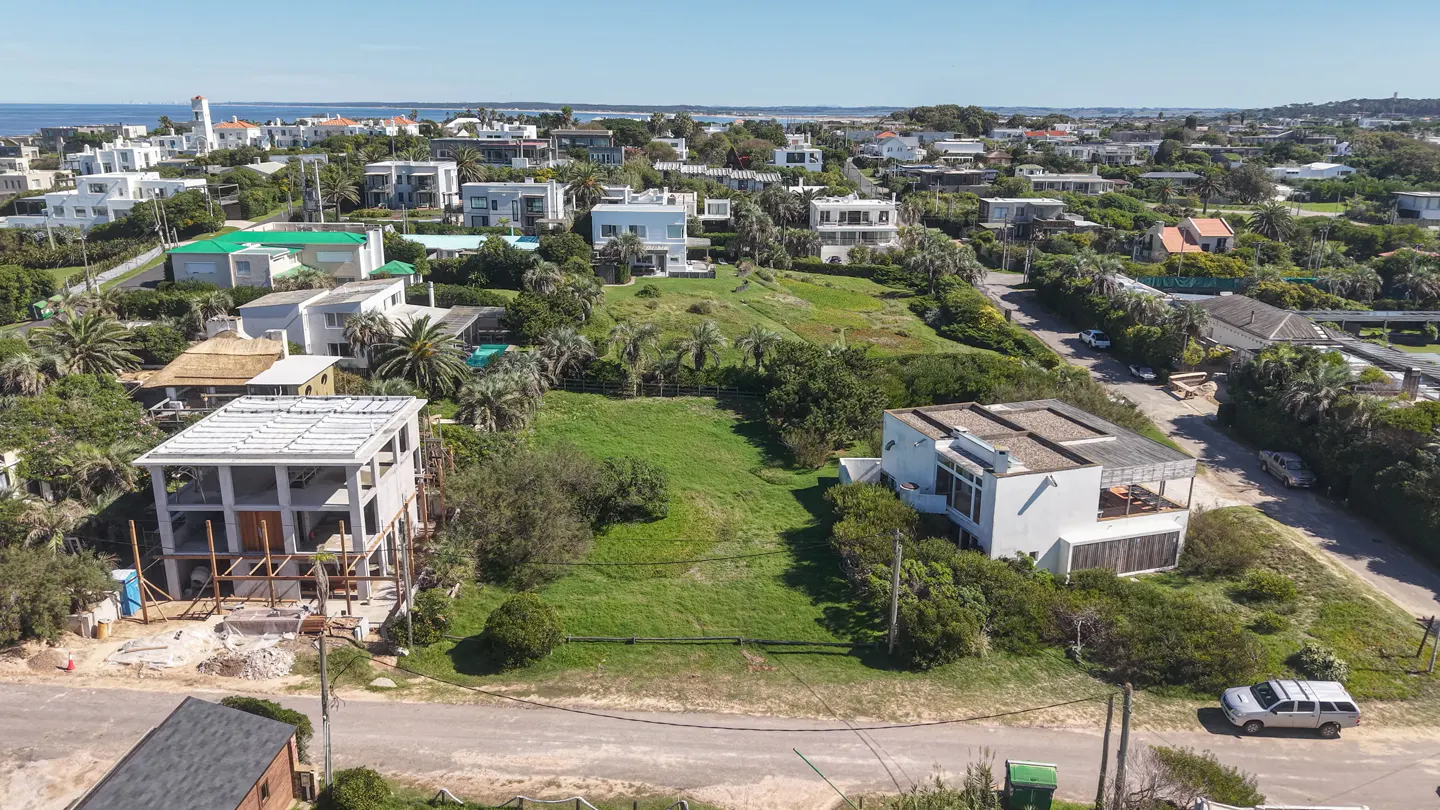 Aerial view of a vacant lot surrounded by houses and greenery, with a white SUV parked nearby.