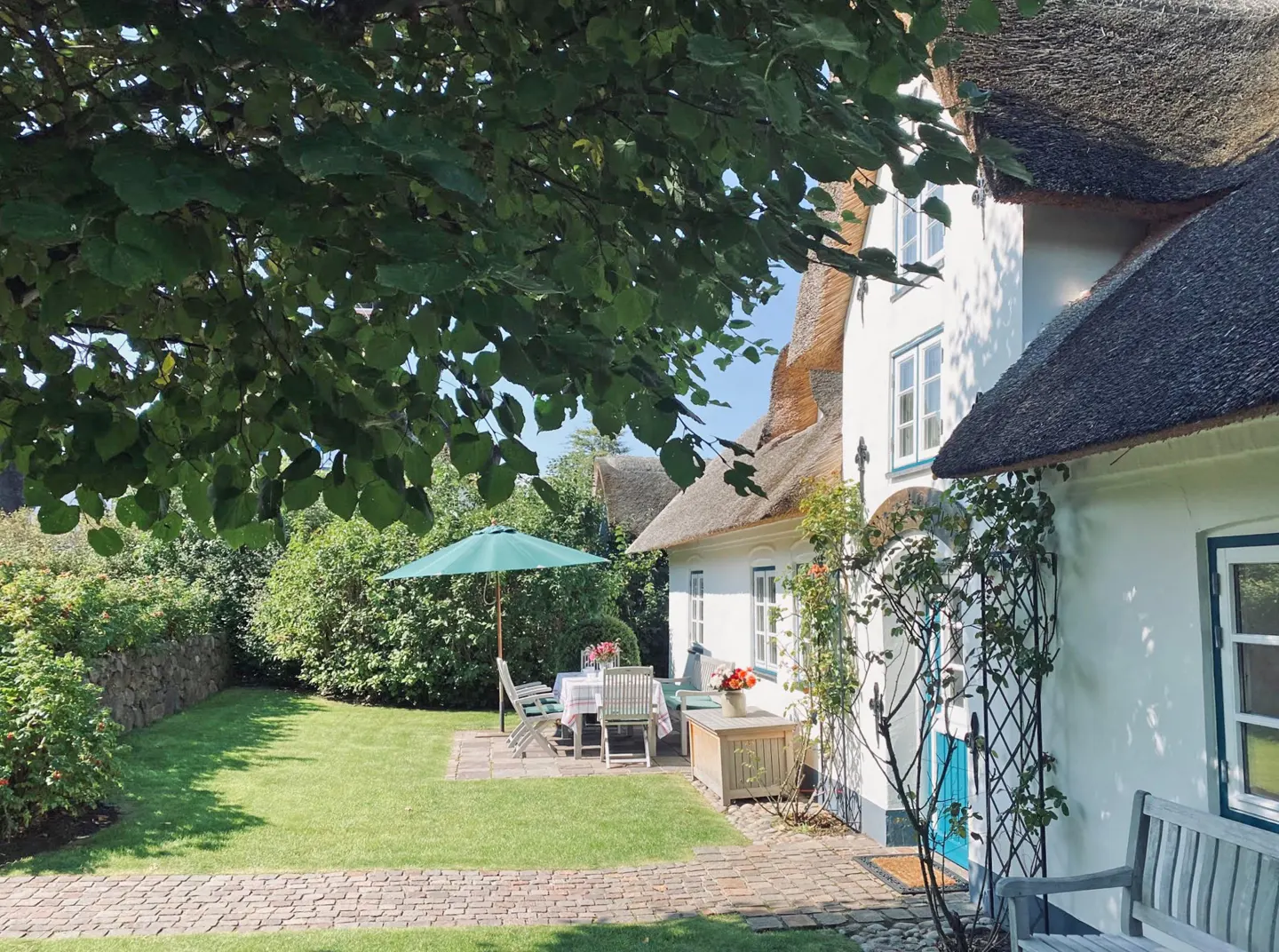 Exterior view of a white house with a thatched roof and a green lawn with patio furniture.