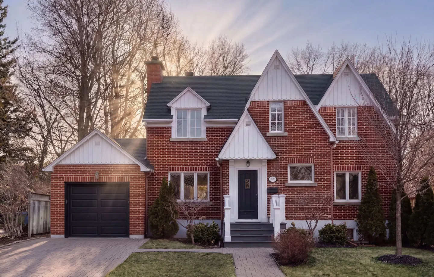 A red brick house with a dark roof, white trim, and a black garage door on a sunny day.