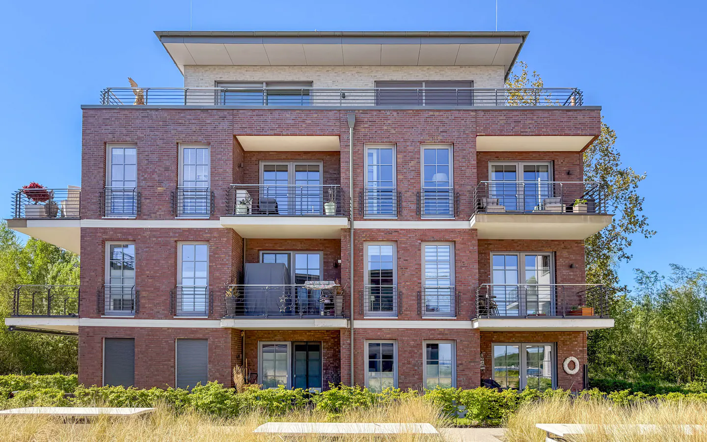 Three-story brick apartment building with balconies and large windows under a clear blue sky.