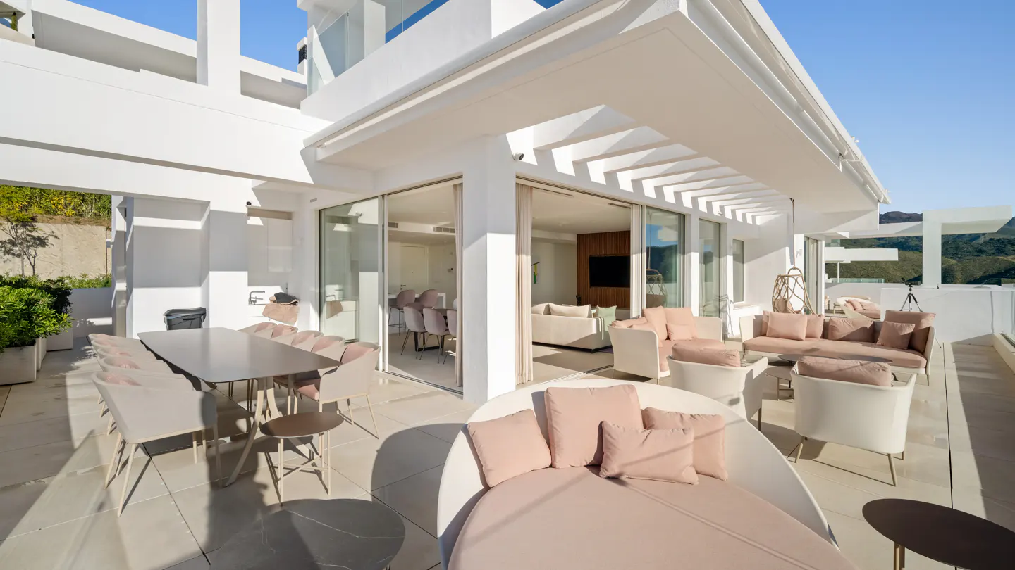 Luxury white patio with dining table, lounge seating, and daybed. Sliding glass doors lead to the interior. Mountain view in the background.