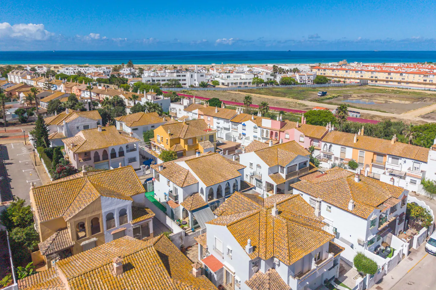 Aerial view of a residential area with white houses and orange tile roofs near a beach and blue ocean.
