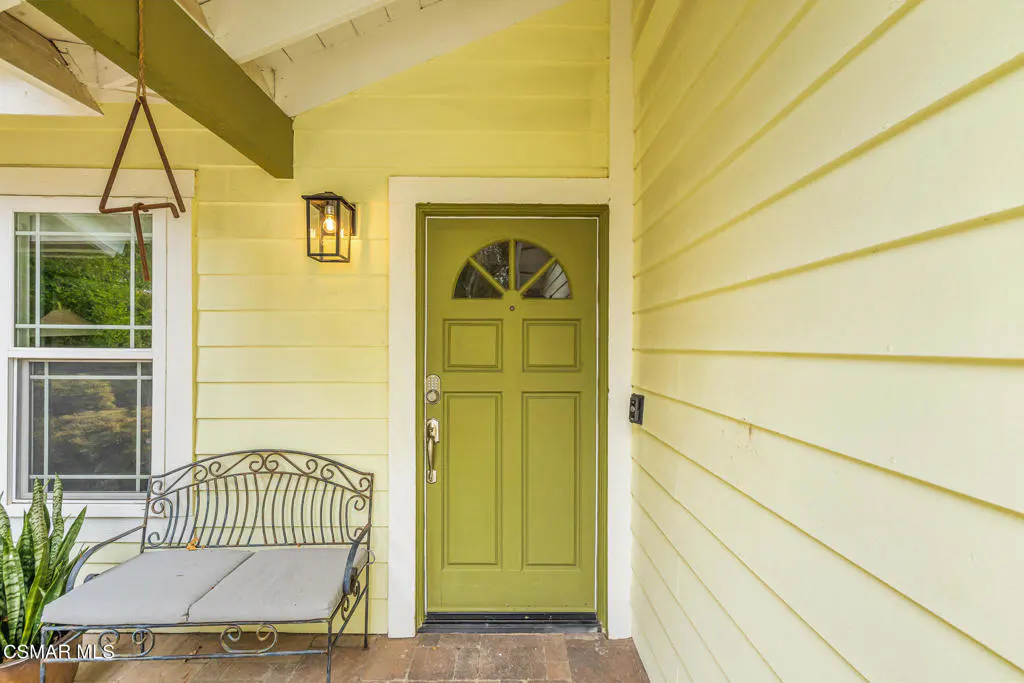 Exterior of a yellow house with a green front door, a bench, and a window.