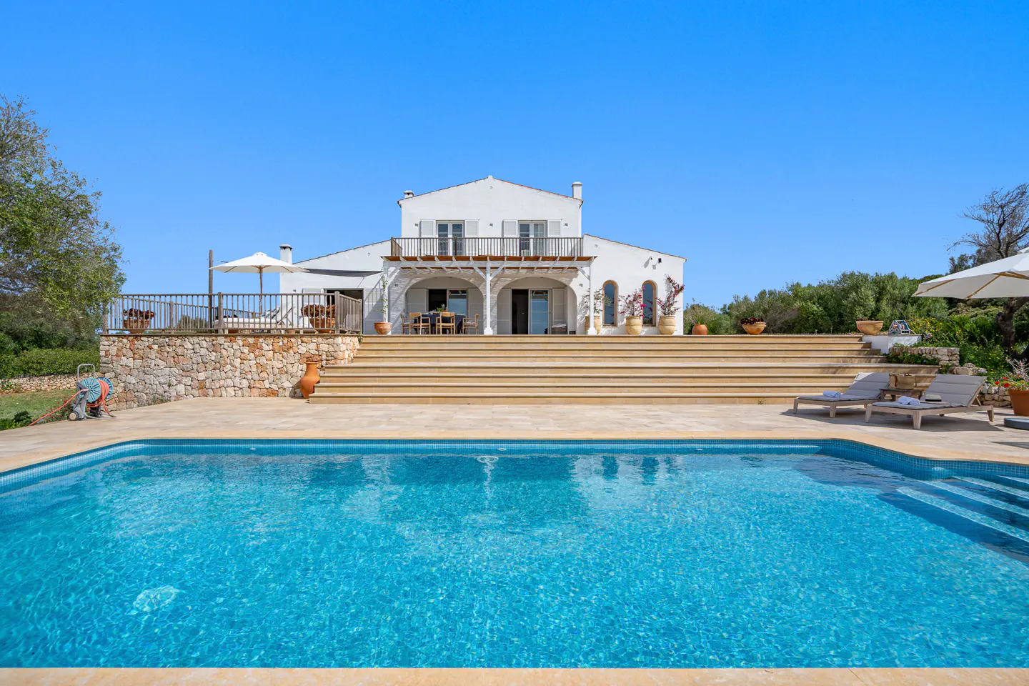 Exterior of a two-story white house with a pool in the foreground under a clear blue sky.