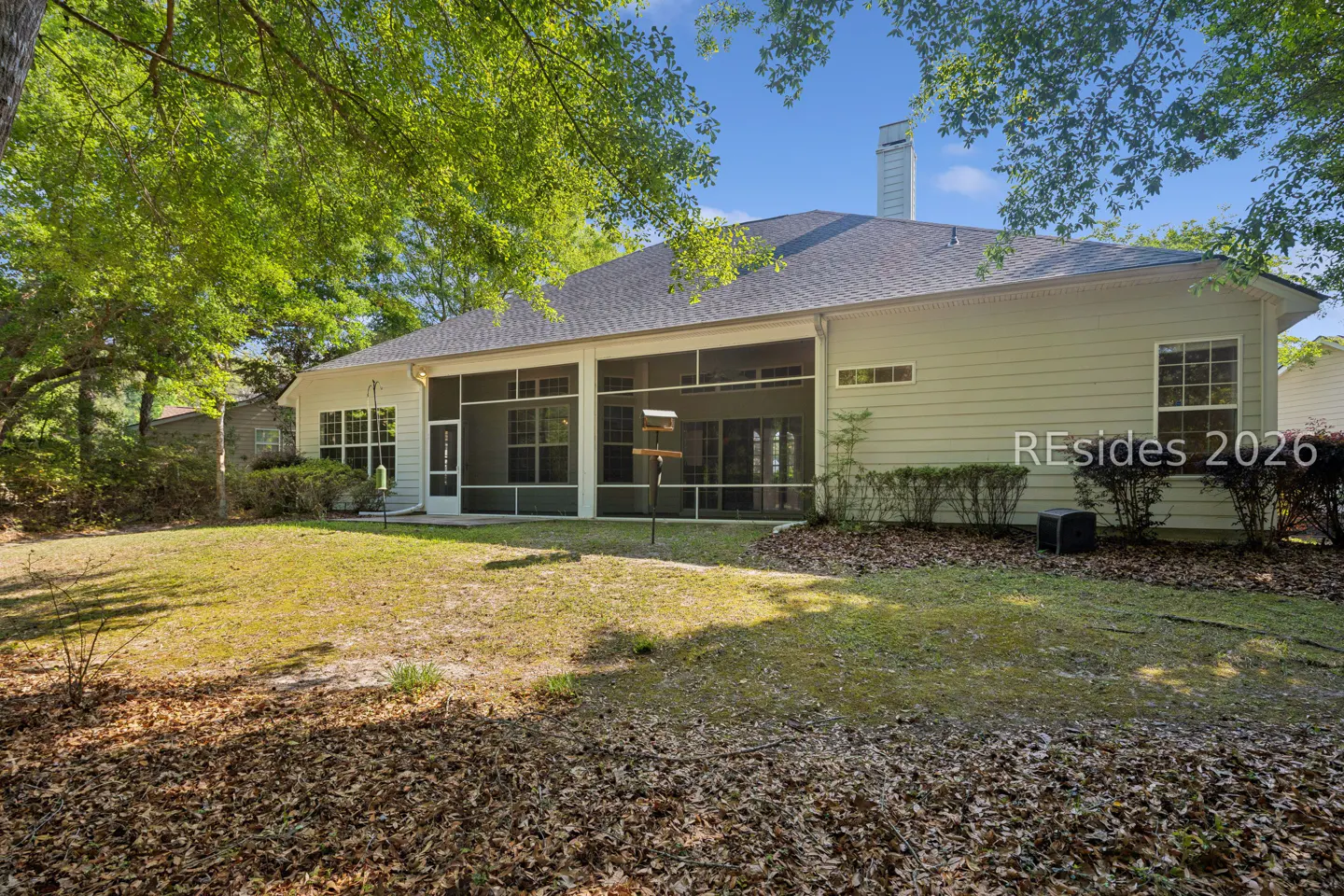 Backyard view of a light green house with a screened-in porch, a bird feeder, and a chimney.