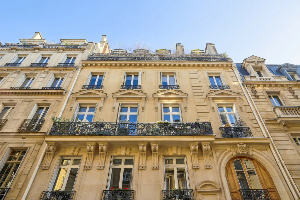 Exterior view of Parisian apartment buildings with wrought iron balconies and blue sky.