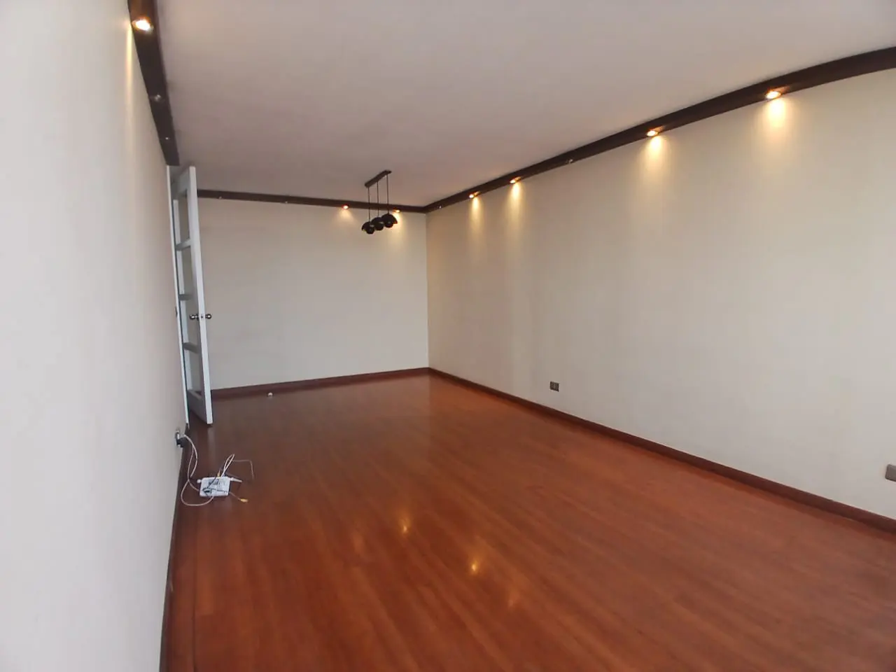 Empty room with polished wood floors, cream walls, recessed ceiling lighting, and a modern three-bulb pendant fixture.