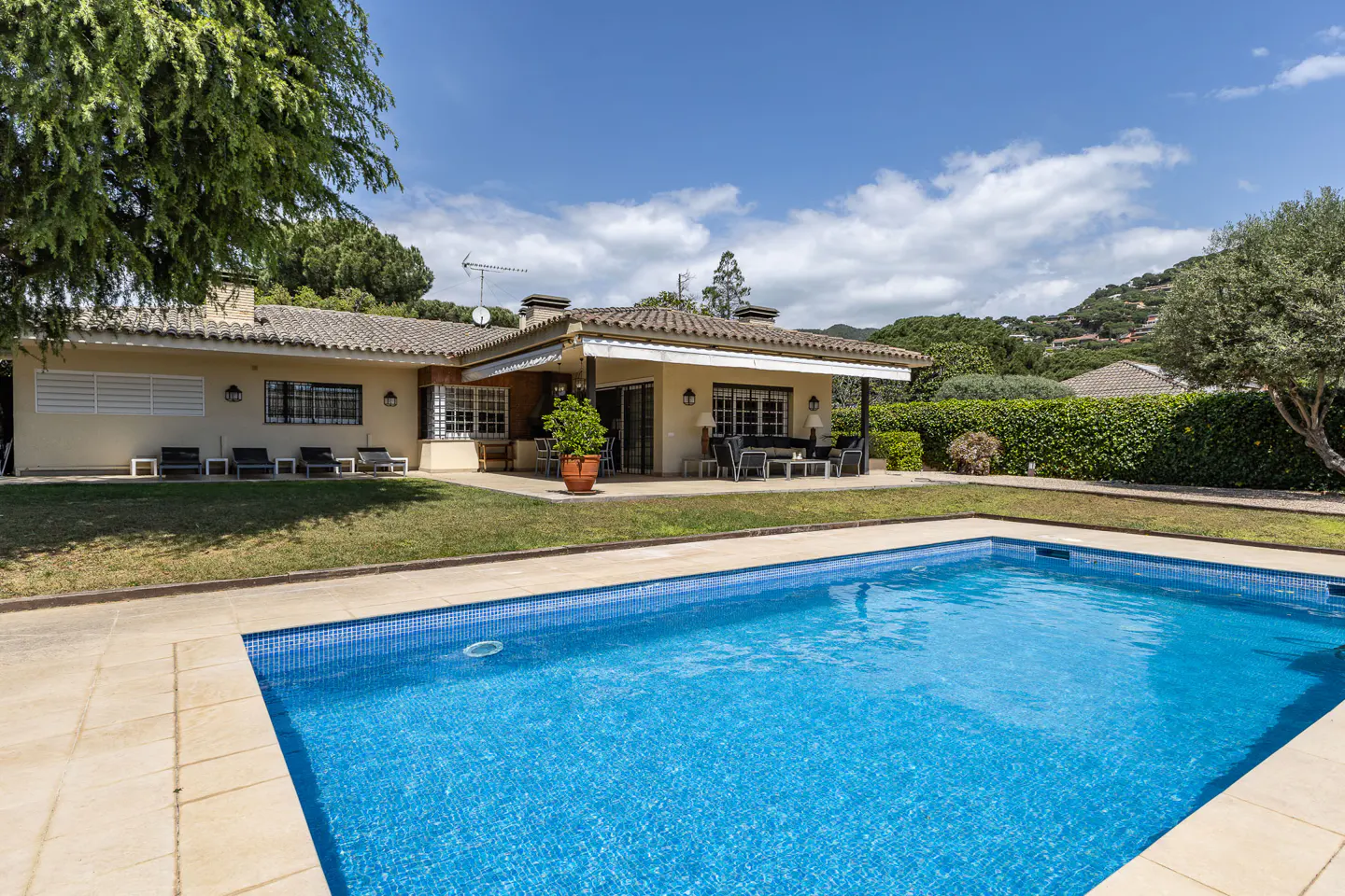 A tan house with a blue tiled pool in the foreground on a sunny day.
