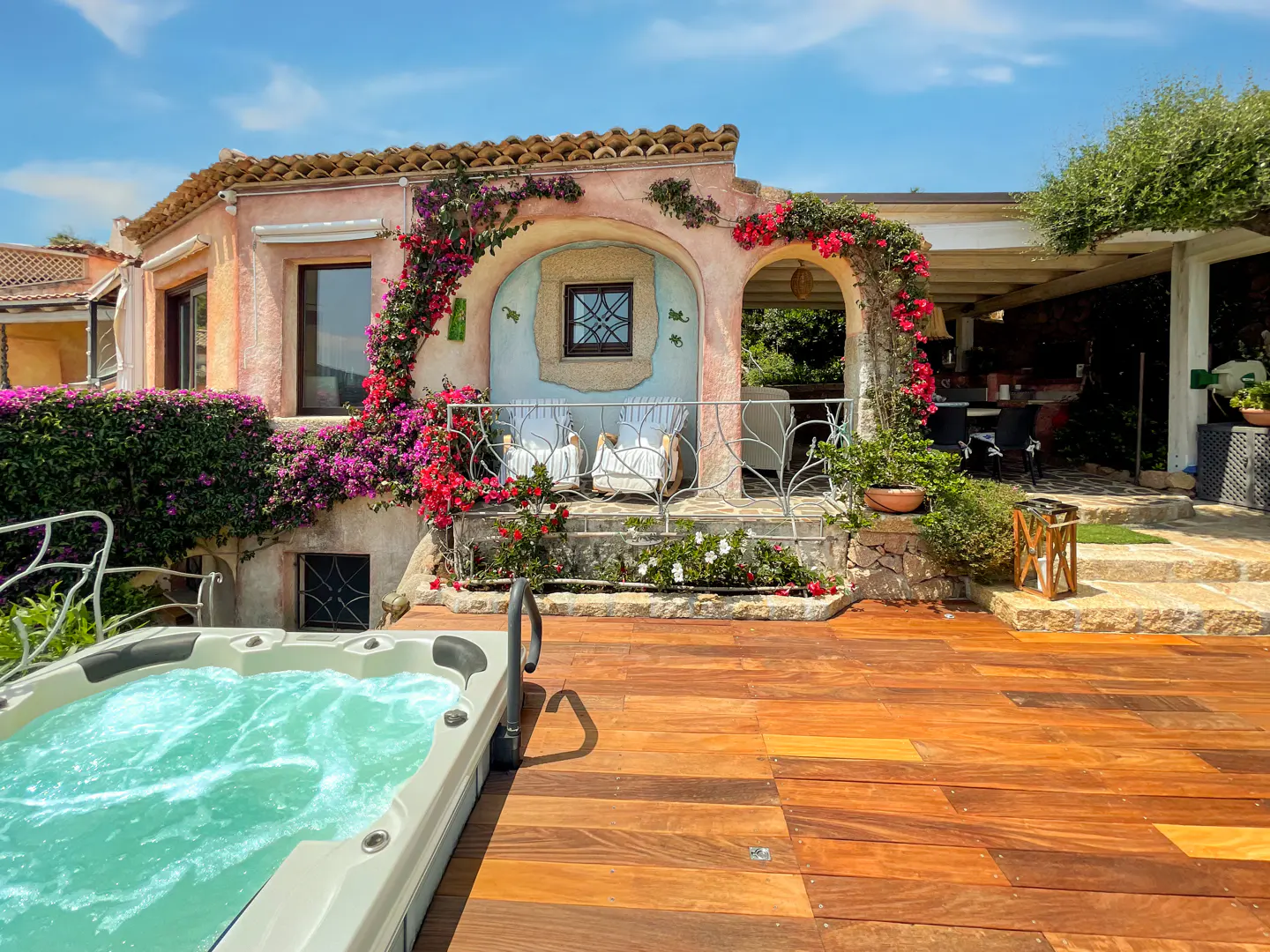 Exterior view of a pink stucco house with a hot tub and a wooden deck. Bougainvillea climbs the walls.