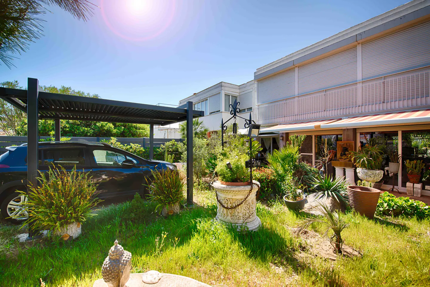 Exterior of a modern home with a black car under a pergola, lush green lawn, and potted plants.