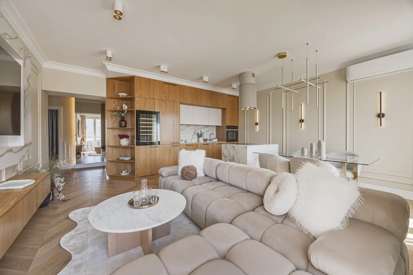 Open-concept living space with a beige sectional sofa, marble coffee table, and wood cabinets in the kitchen area.