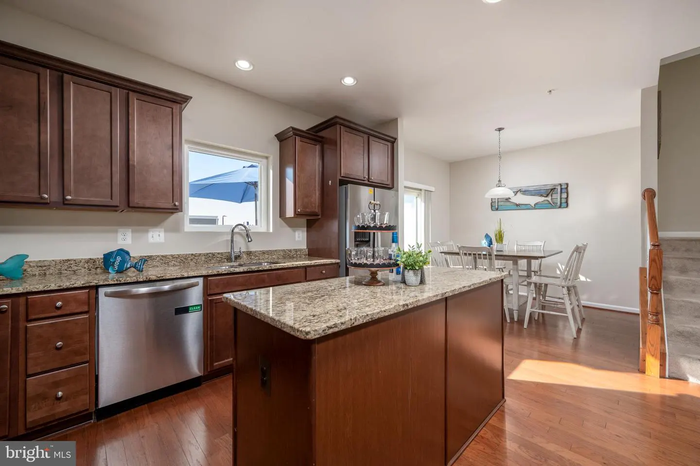 A kitchen with brown cabinets, granite countertops, and stainless steel appliances. A kitchen island is in the center, and a dining area is visible in the background.