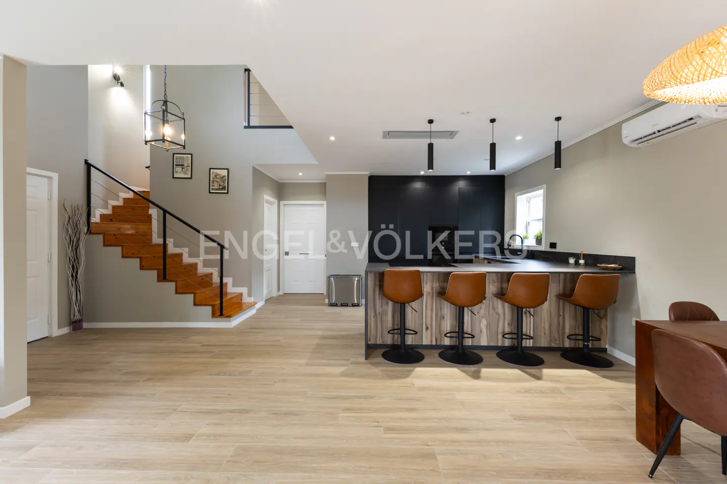 Open-concept living space with wood floors, stairs, and a kitchen island with brown leather stools.