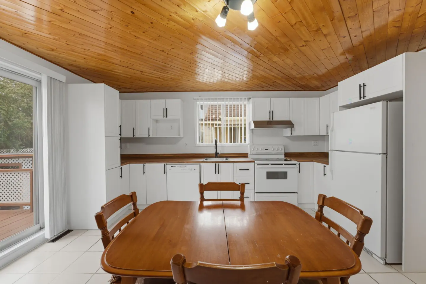 A kitchen with white cabinets, a wood countertop, and a wood ceiling. A wood table with chairs is in the foreground.