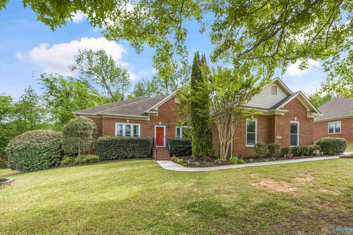 A single-story red brick house with a red front door, green lawn, and trees under a blue sky.