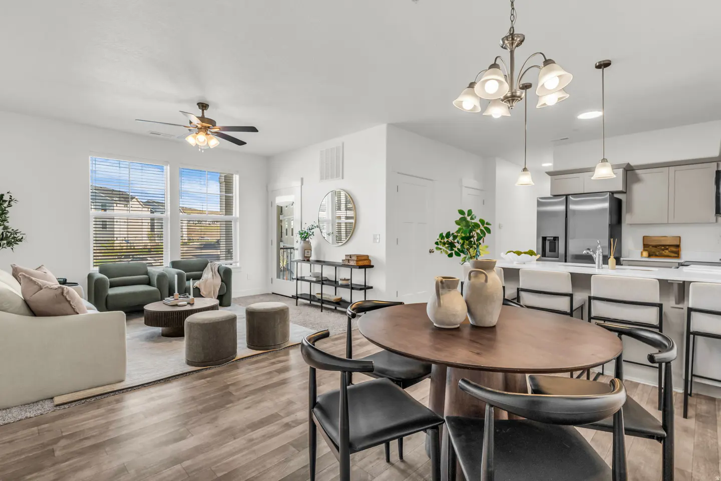 Open-concept living space with a dining table, chairs, and a living room with a sofa and armchairs. The kitchen has a white countertop.
