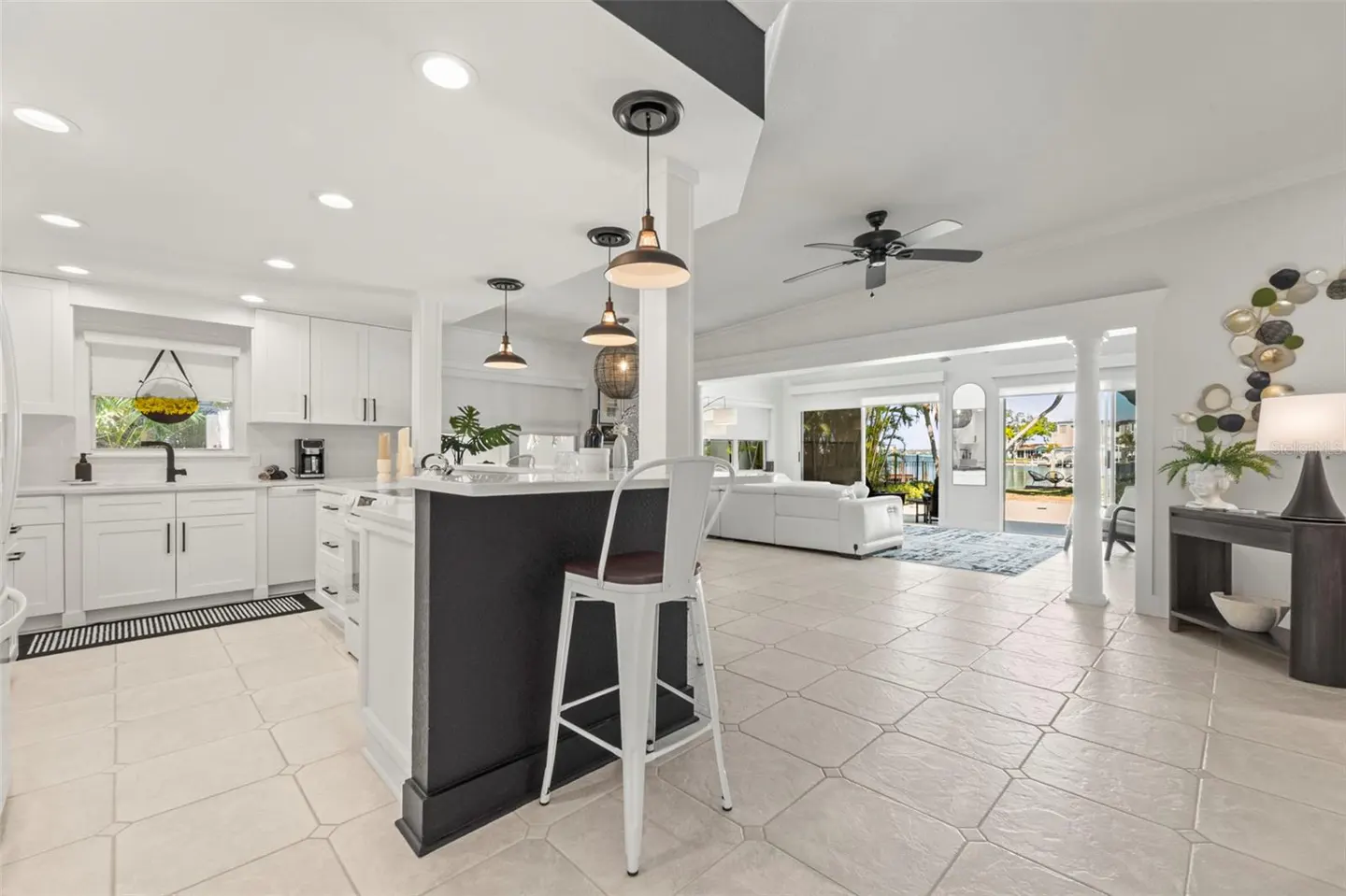 Bright, open-concept kitchen and living room with white cabinets, black island, and view of the water.