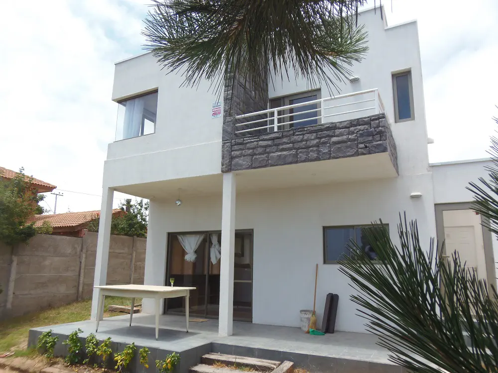 Two-story white house with gray stone accents, a balcony, and a patio with a white table.