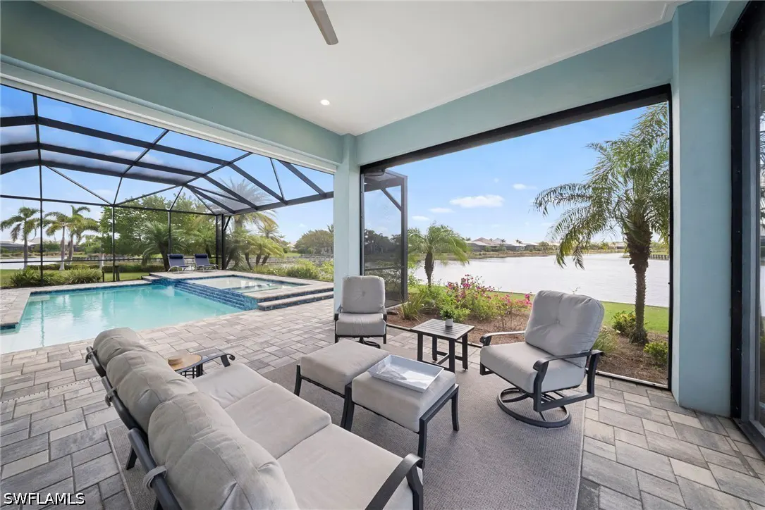 Screened-in patio with gray furniture overlooking a pool, palm trees, and a lake on a sunny day.
