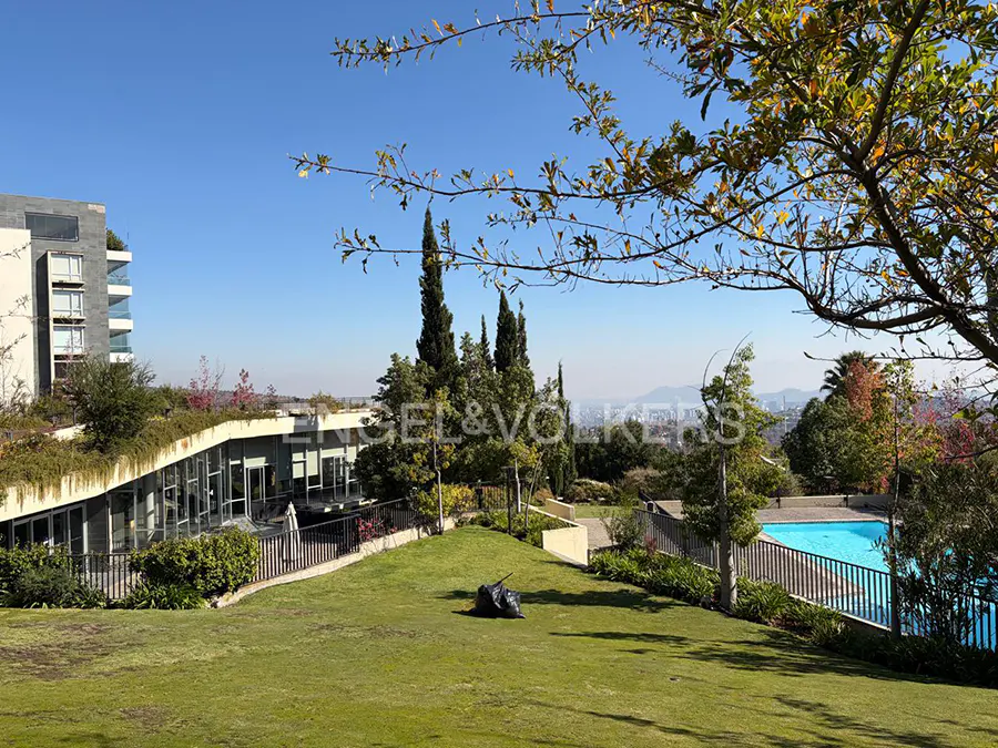 Lush green lawn with modern building, pool, and city view under a blue sky. Trees frame the scene.