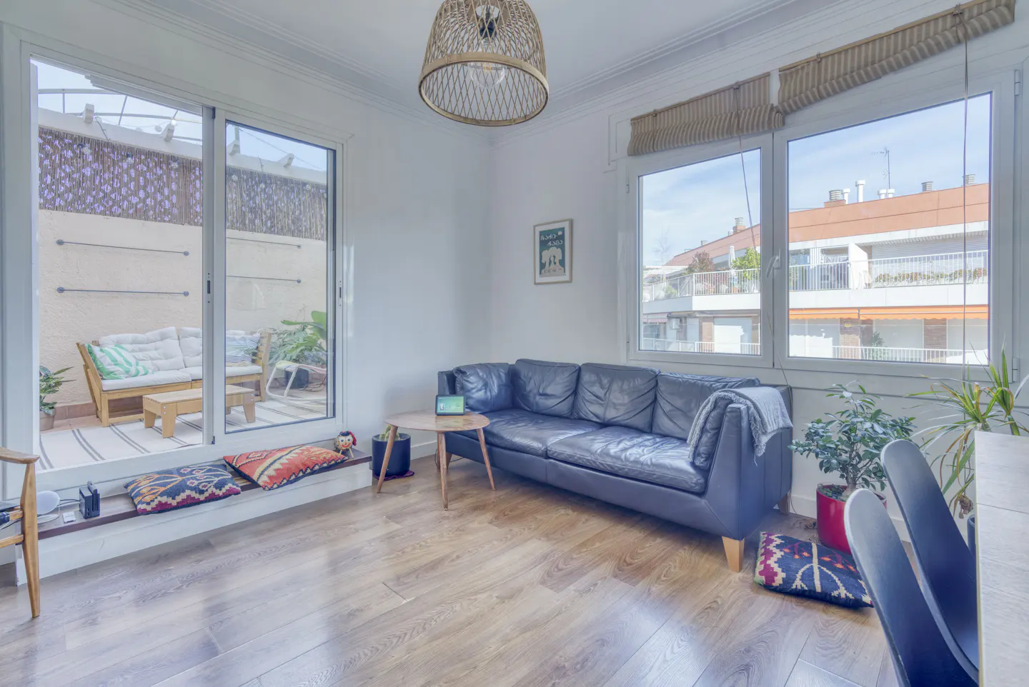 Bright living room with wood floors, a blue leather sofa, and a sliding glass door to a patio with outdoor seating.
