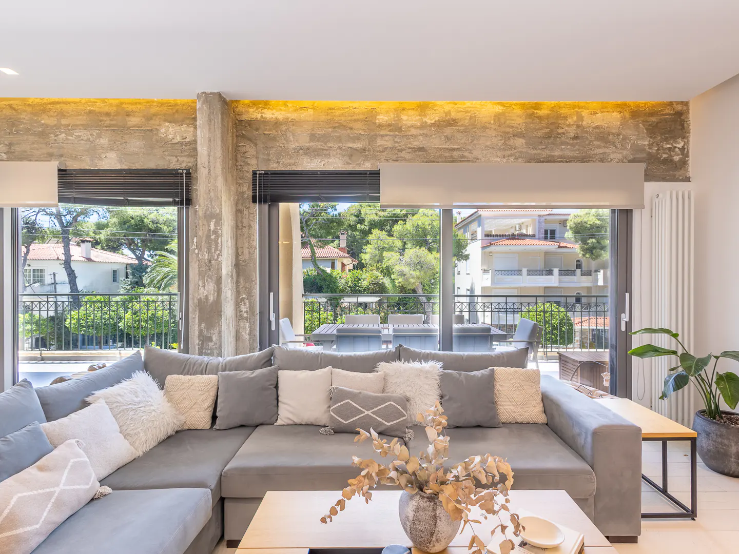 Modern living room with a large grey sectional sofa, coffee table, and floor-to-ceiling windows overlooking a balcony.